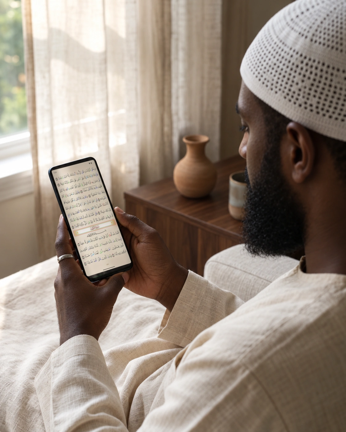 A Somali reader in a kufi holding a phone displaying a real Madinah mushaf page in Criterion.